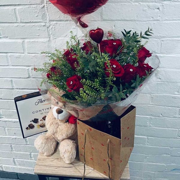 Valentines Day, twelve red roses with teddy bear, box of chocolates and a heart shaped balloon.