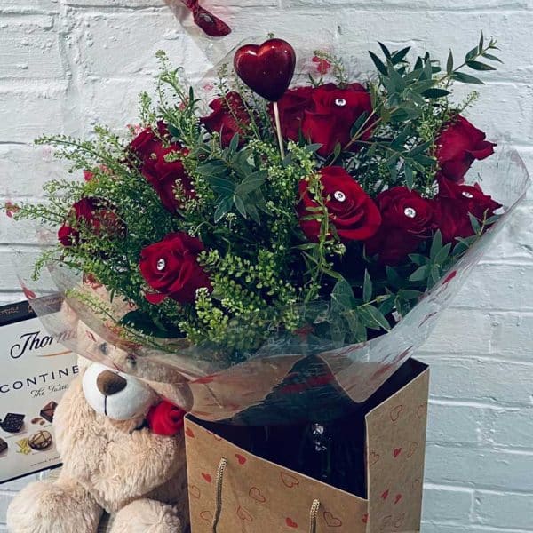 Valentines Day, twelve red roses with teddy bear, box of chocolates and a heart shaped balloon.