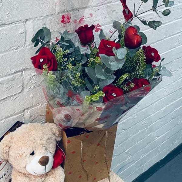 Valentines Day, six red roses with teddy bear, box of chocolates and a heart shaped balloon.